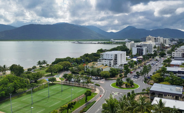 Cairns Australia view of city and mountains tennis court. Cairns Australia a coastal city seen from above with green tennis court, a traffic roundabout, palm trees and mid-rise buildings backed by mountains and a dramatic cloudy sky over the Trinity inlet